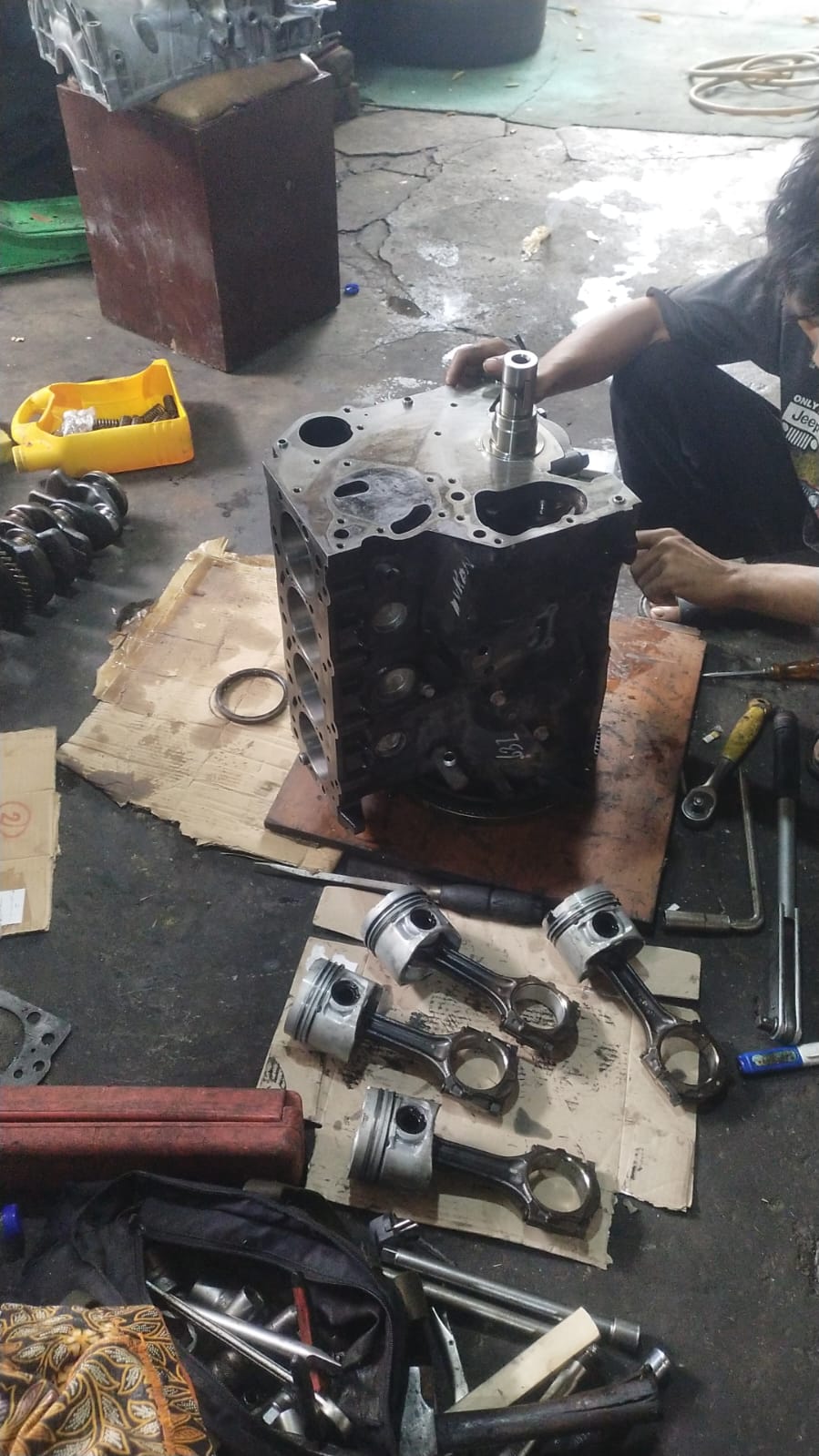 Overhaul blok mesin diesel — piston, connecting rod, dan crankshaft tertata di area kerja
